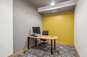A desk with a computer monitor and keyboard sits in a room with a patterned wallpaper.